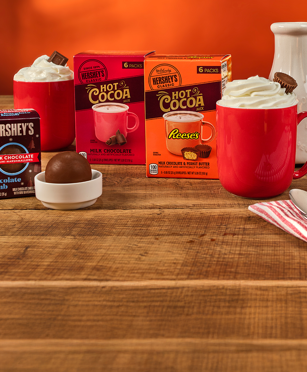 Promotional graphic featuring assorted flavors of hot cocoa boxes on a wooden tabletop