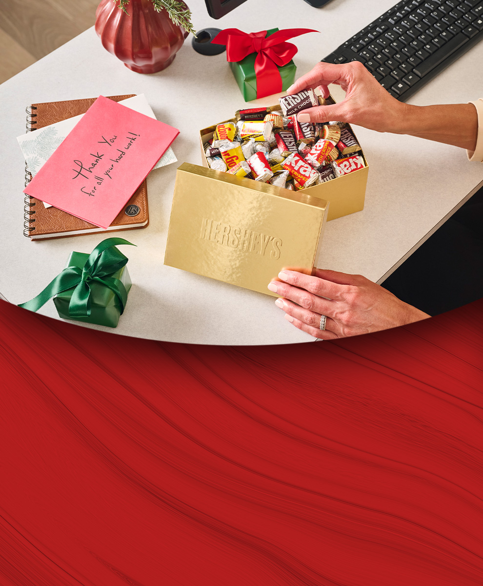 Promotional graphic showing an office worker reaching towards a HERSHEY'S Golden Gift Box to pick up a piece of candy