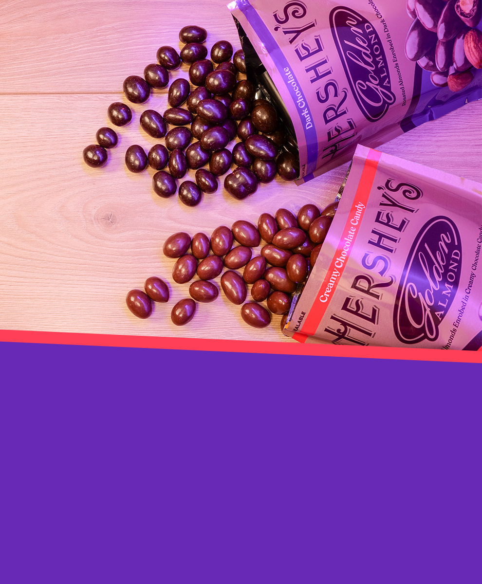 Promotional graphic featuring HERSHEY'S GOLDEN ALMOND Chocolate Covered Almond pouches spilling open onto a tabletop