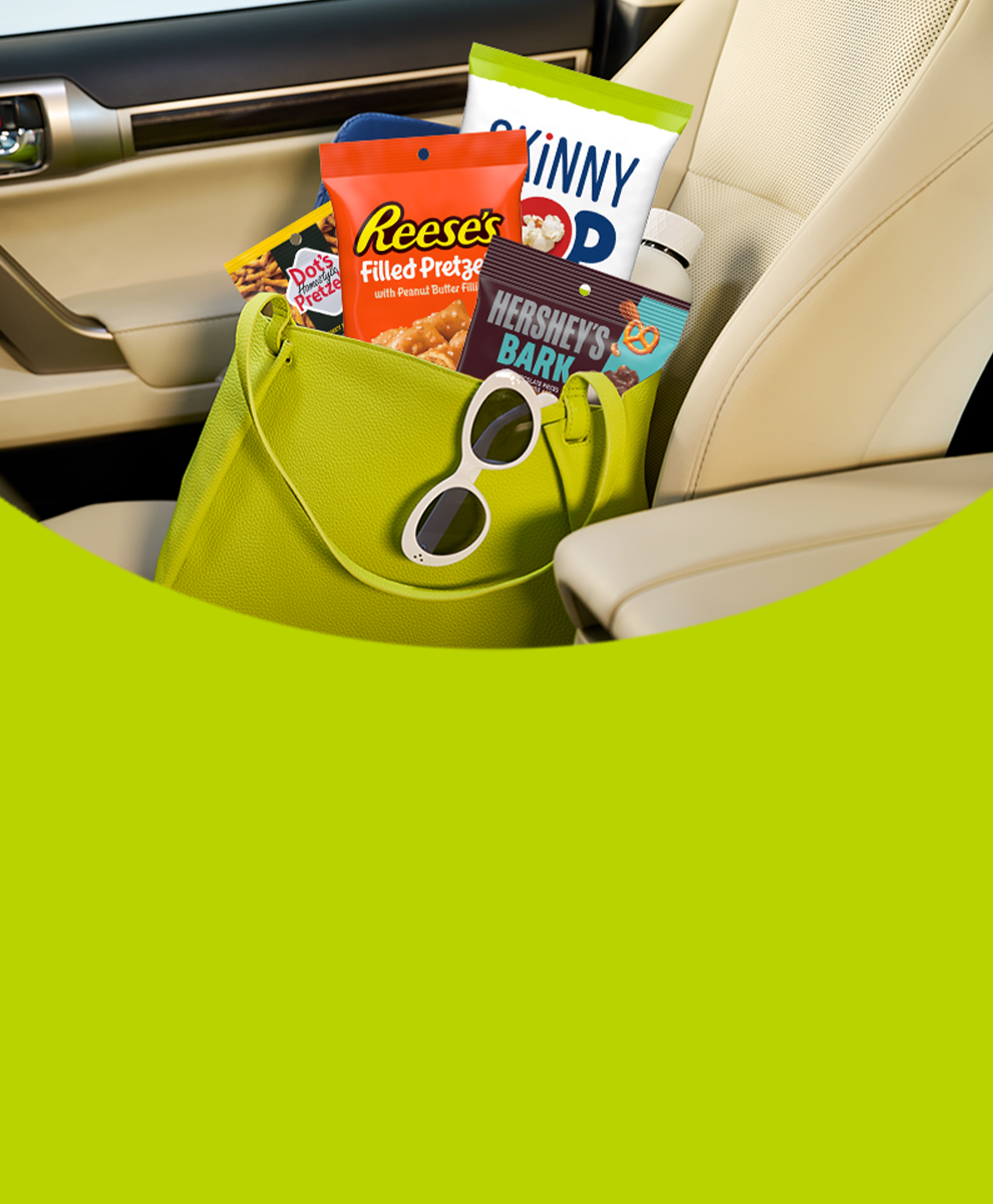 Assorted HERSHEY'S and REESE'S and DOT'S and SKINNYPOP individually sized bags in a purse sitting in the passenger seat of a car
