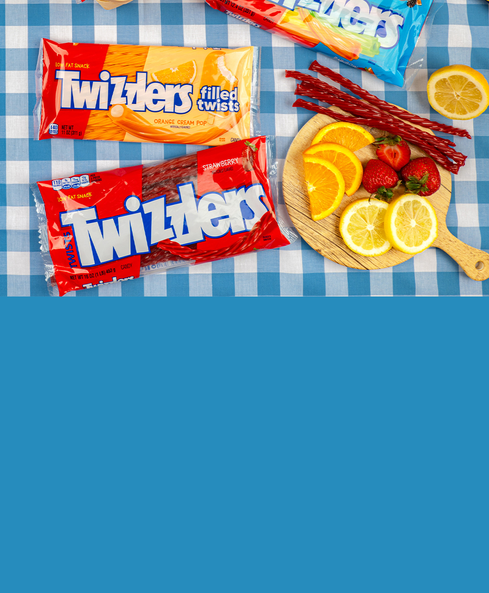 TWIZZLERS filled and classic candy bags on a picnic blanket alongside freshly cut fruit