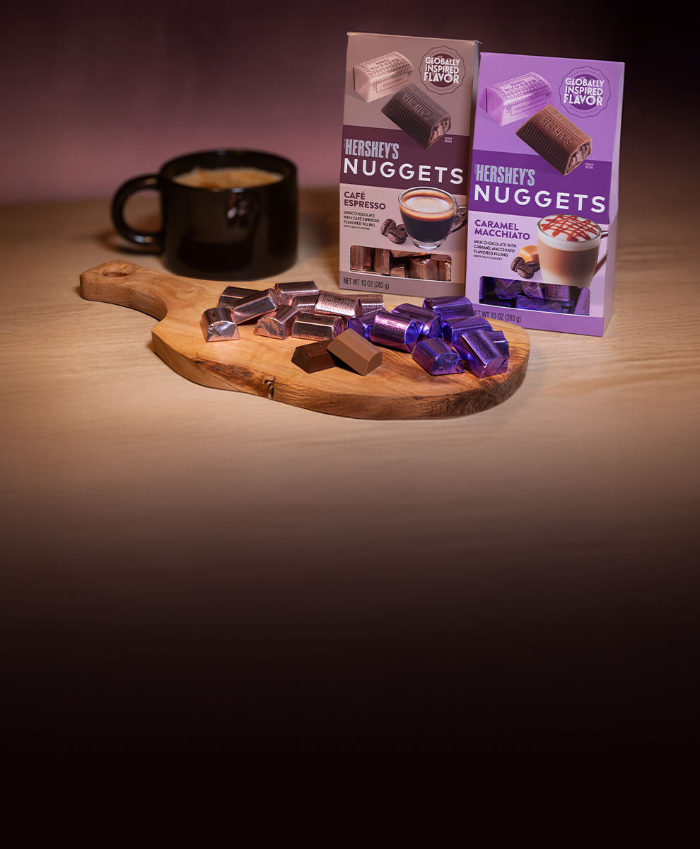 HERSHEY'S Nuggets chocolate in caramel macchiato and cafe espresso flavors next to a cup of coffee on a wooden serving tray