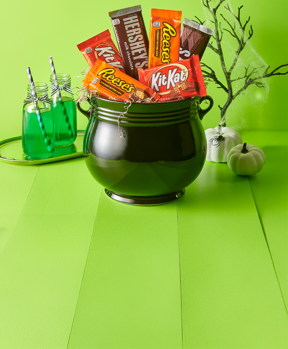 Promotional graphic featuring assorted full size HERSHEY'S and REESE'S and KIT KAT® candy bars in a pumpkin-shaped bowl