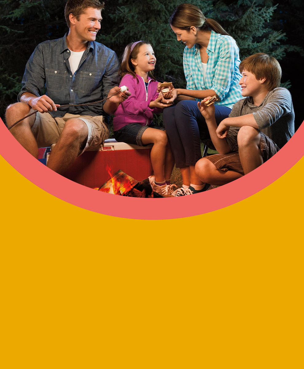 Family gathered around a bonfire eating s'mores