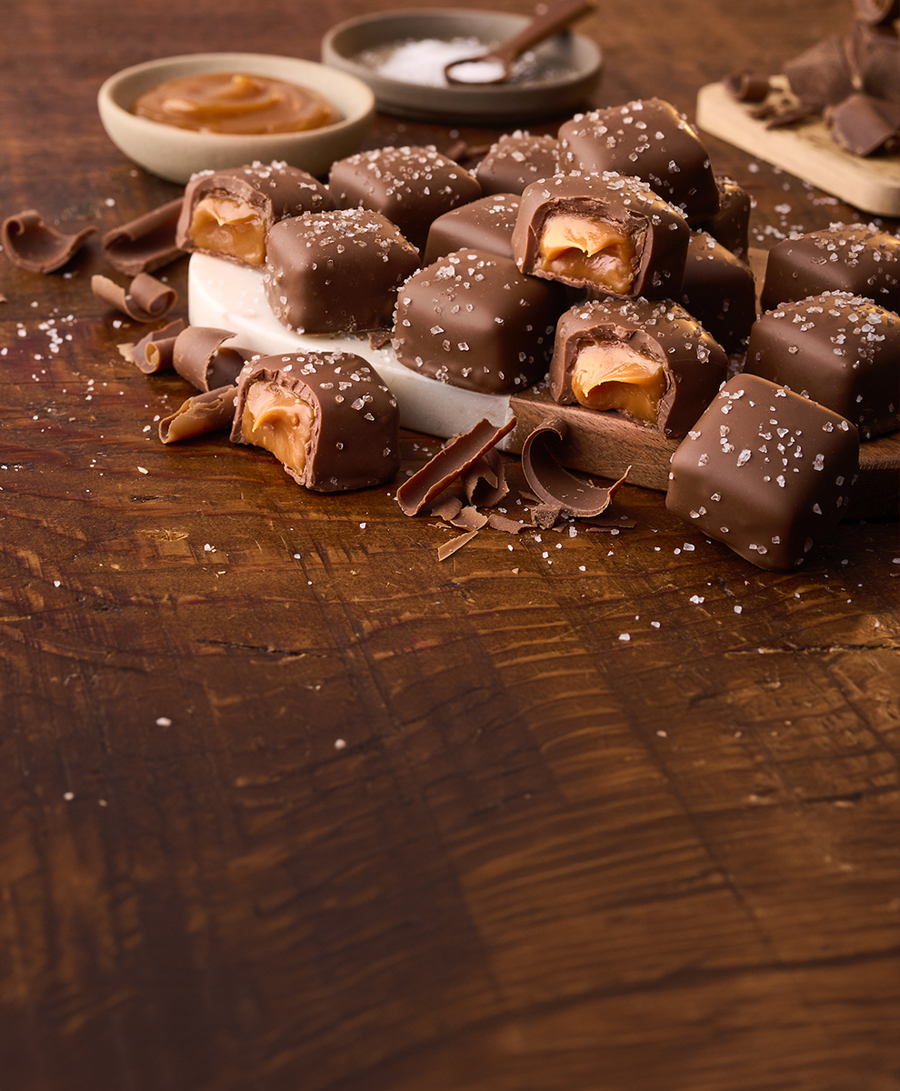 HERSHEY'S Caramels stacked on top of a serving board on a wooden table