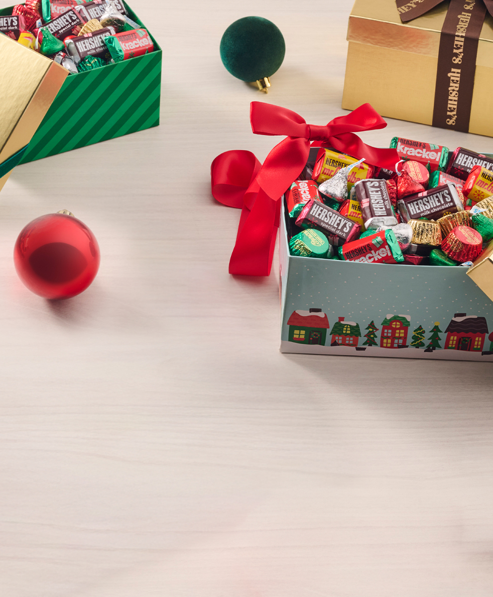 Promotional graphic featuring gold and seasonal HERSHEY'S gift boxes filled with assorted candies