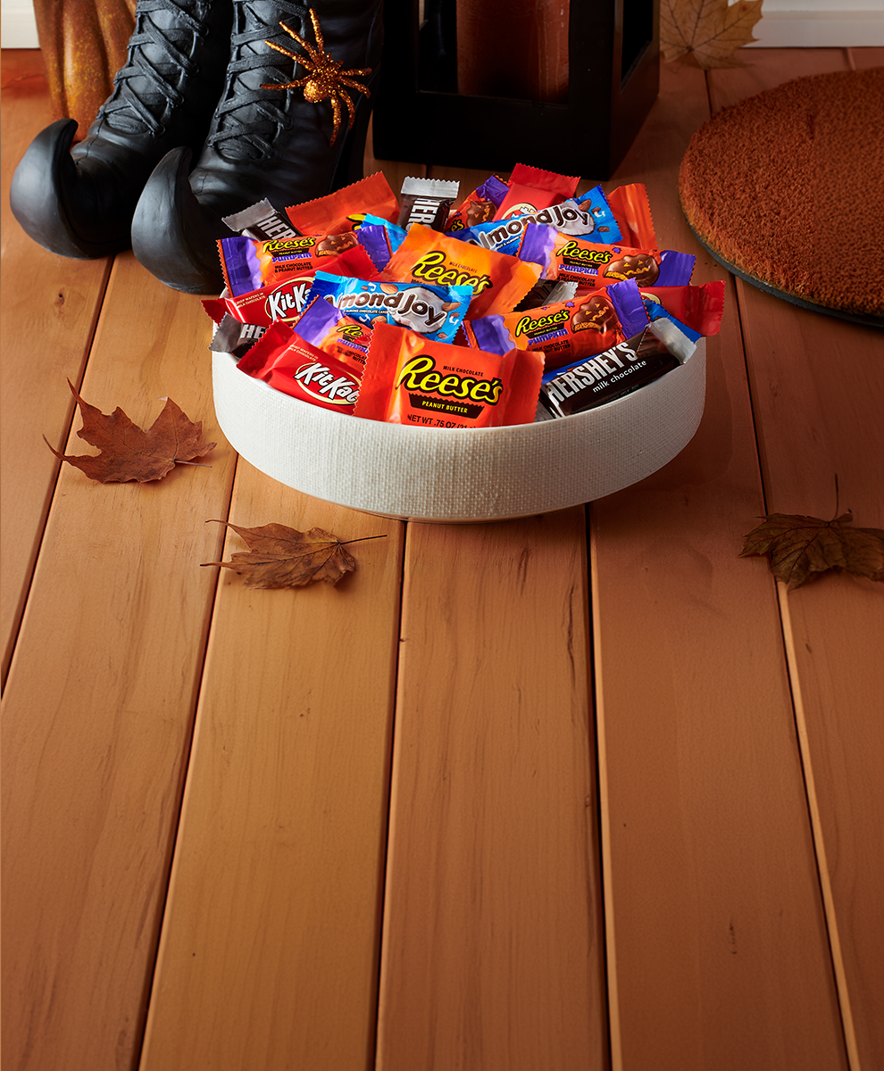 Promotional graphic featuring assorted snack size candies in a trick-or-treat bowl on a porch