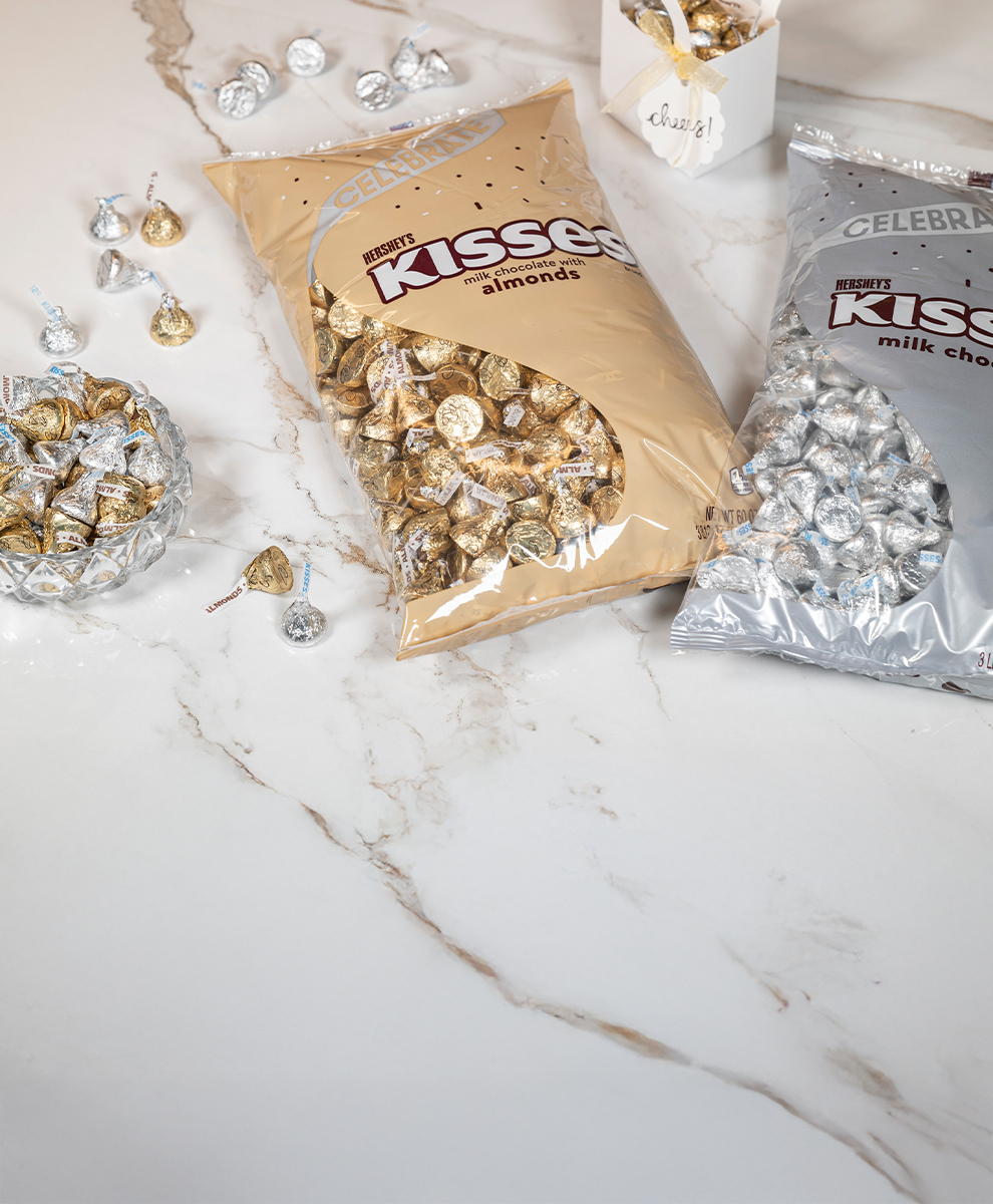 Promotional graphic featuring HERSHEY'S KISSES in silver and gold wrappers spilling out onto a marble countertop
