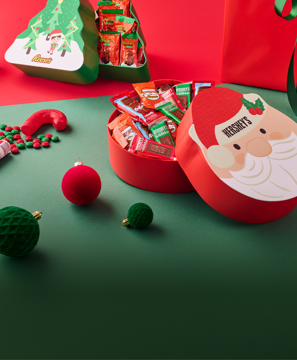 Promotional graphic featuring assortment of HERSHEY'S and REESE'S and KIT KAT® holiday and christmas candy boxes and gifts on a red and green background
