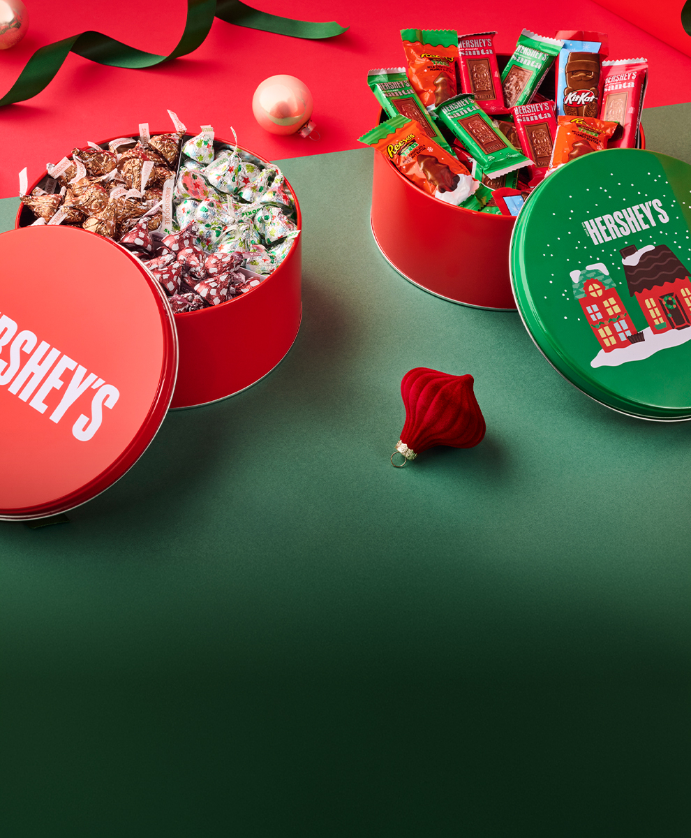 Promotional graphic featuring assortment of HERSHEY'S gift tins on a red and green background