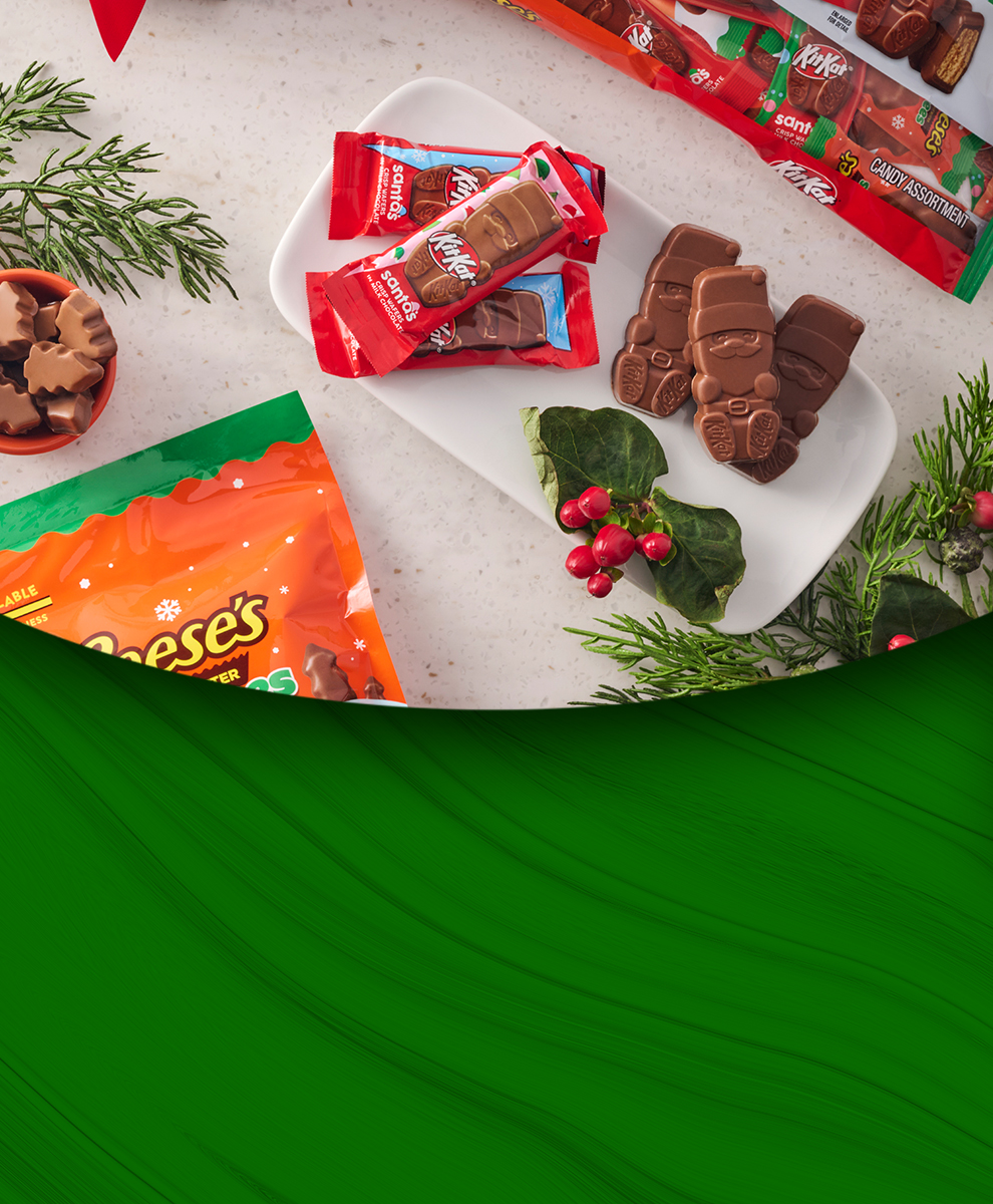 Promotional graphic featuring REESE'S Peanut Butter Trees and KIT KAT® Santas on a marble countertop