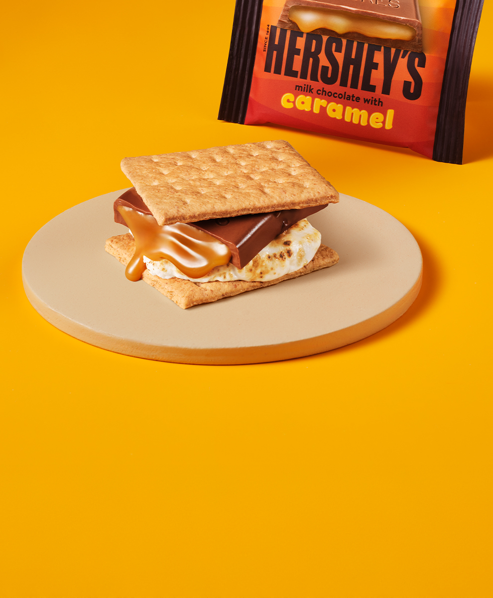 Promotional graphic featuring a s'more made with a HERSHEY'S Milk Chocolate with Caramel bar sitting on a plate