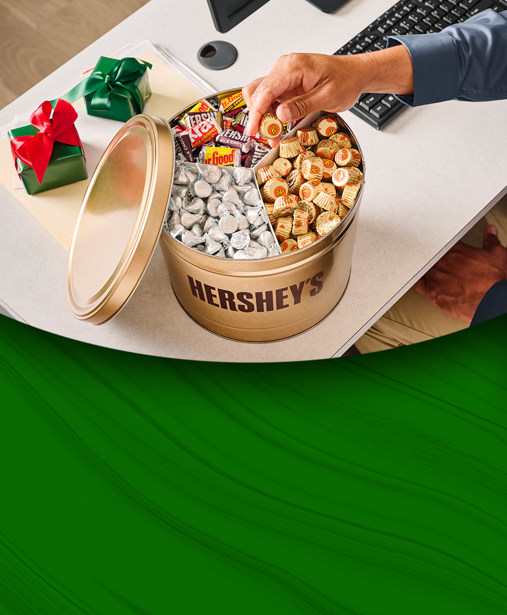 Promotional graphic showing an office worker reaching for a piece of candy from a HERSHEY'S Gold Gift candy tin at their desk