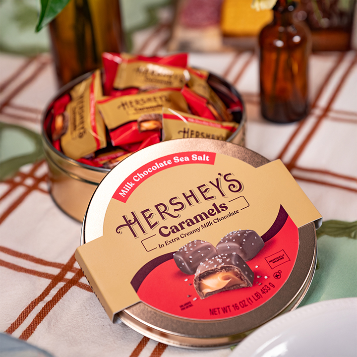 HERSHEY'S Caramels-filled gift tin displayed partially open on a table with a plaid tablecloth