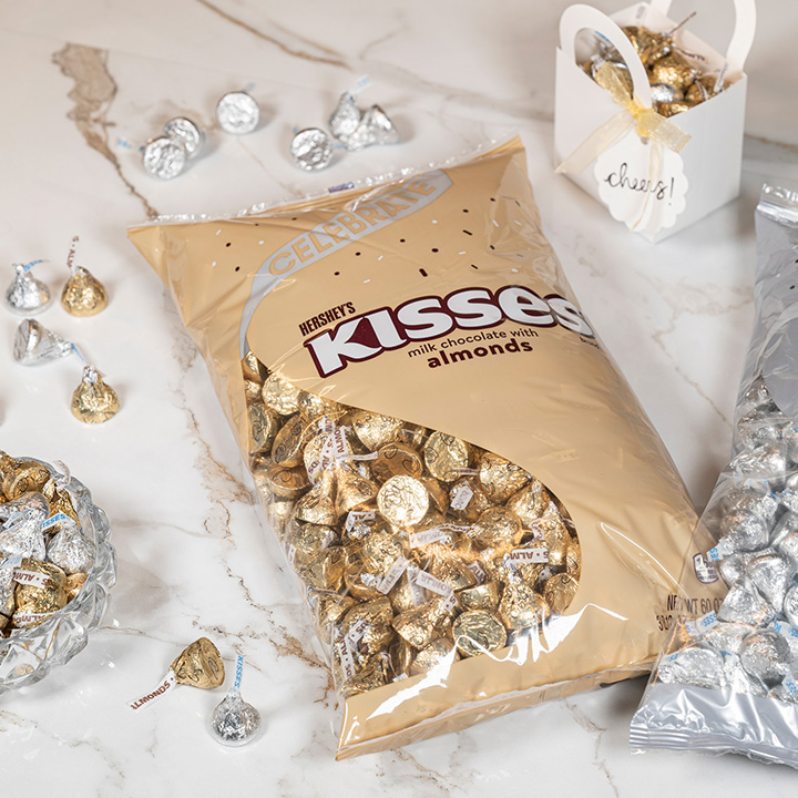 Bulk bags of HERSHEY'S KISSES wrapped in gold and silver foils on a tabletop