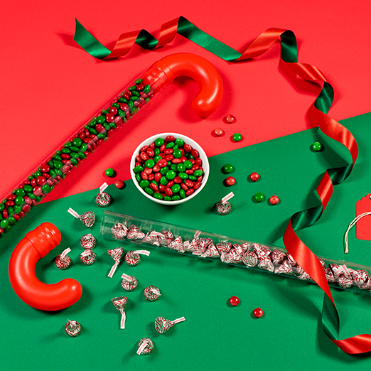 Jumbo plastic canes filled with HERSHEY-ETS candies and HERSHEY'S KISSES spilling out onto a red and green surface