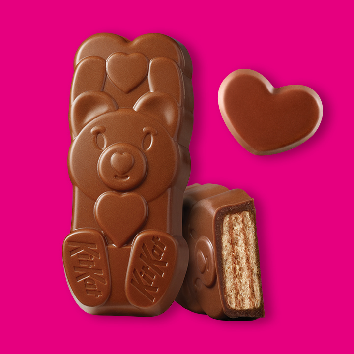 Promotional graphic featuring KIT KAT® milk chocolate bears and REESE'S milk chocolate peanut butter hearts on a pink background