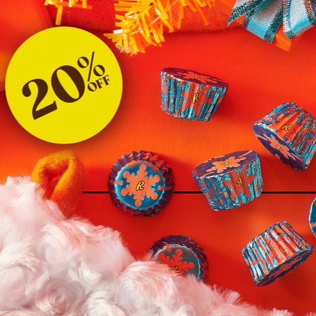 Promotional graphic featuring a REESE'S Sugar Cookie Miniature Peanut Butter Cups spilling out of a Christmas stocking onto an orange tabletop