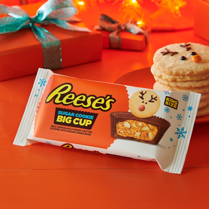 Promotional graphic featuring a pack of REESE'S Sugar Cookie Peanut Butter Cups next to a stack of sugar cookies