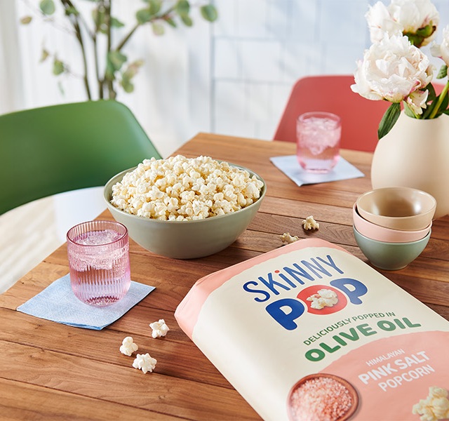 Promotional graphic featuring SKINNYPOP Olive Oil on a dinning room table as a snack