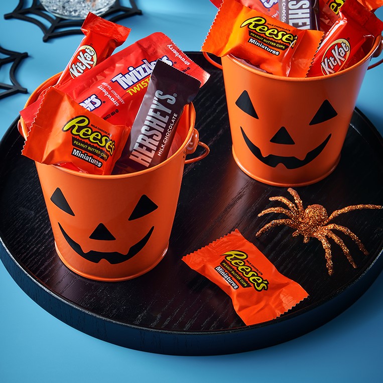 Promotional graphic featuring assorted snack size individually wrapped candies in trick-or-treat themed pails