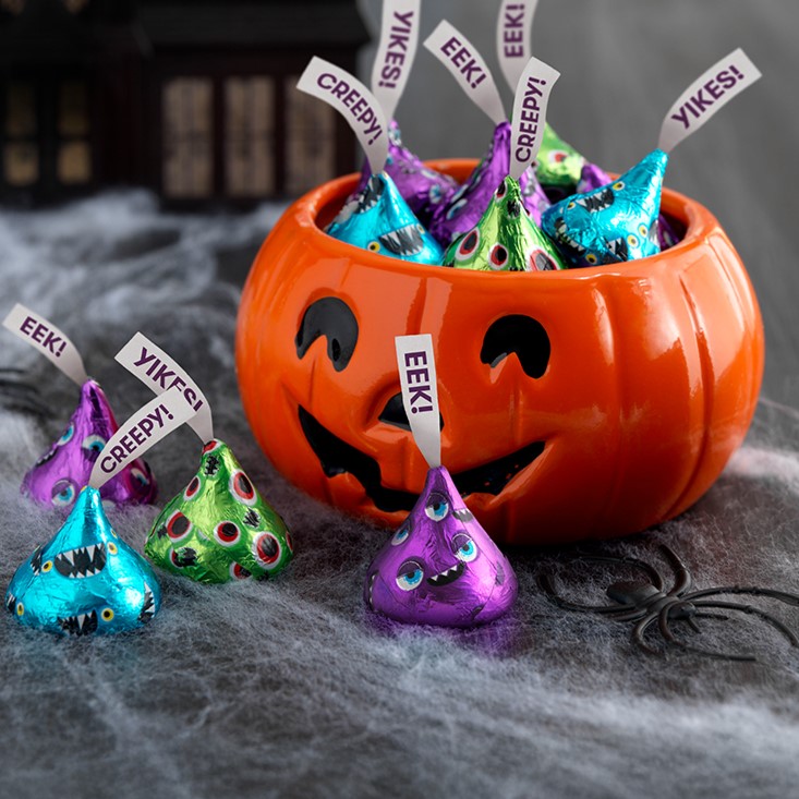 Promotional graphic featuring HERSHEY'S Kisses with Monster themed foils in a jack-o-lantern bowl