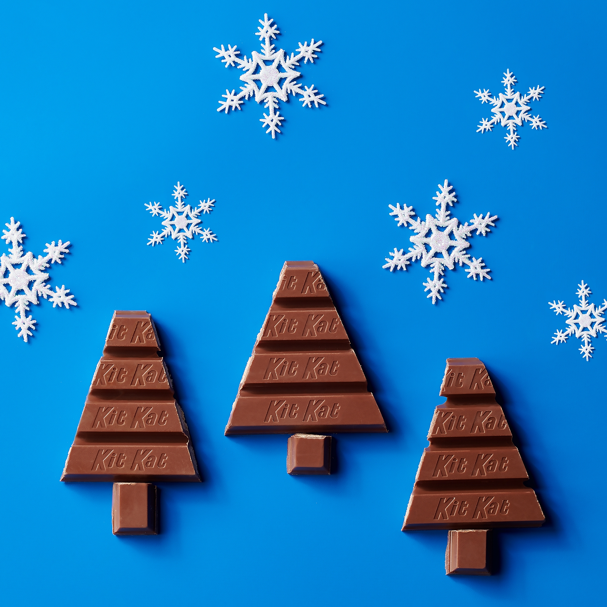 Promotional graphic featuring KIT KAT chocolate candies broken into Christmas tree shapes on a blue background