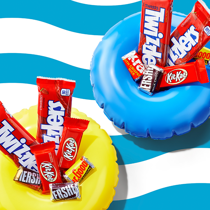 Assorted HERSHEY'S and KIT KAT® and REESE'S Chocolates on a blue background alongside flowers