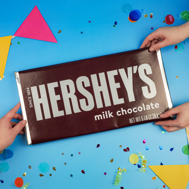 Promotional graphic featuring hands grabbing a HERSHEY'S World's Largest chocolate bar