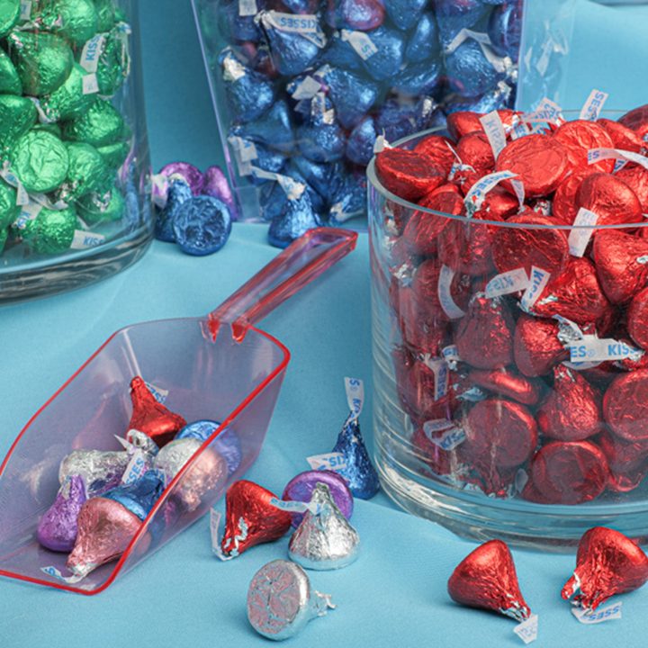 Glass jars and scoopers filled with HERSHEY'S KISSES in red blue purple and green foils