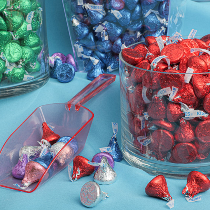 HERSHEY'S KISSES wrapped in red and green and blue foils in assorted glass jars on a tabletop