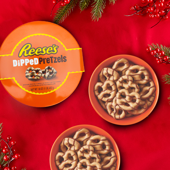 REESE'S Dipped Pretzel Gift Tin on a holiday-decorated tabletop with a red tablecloth