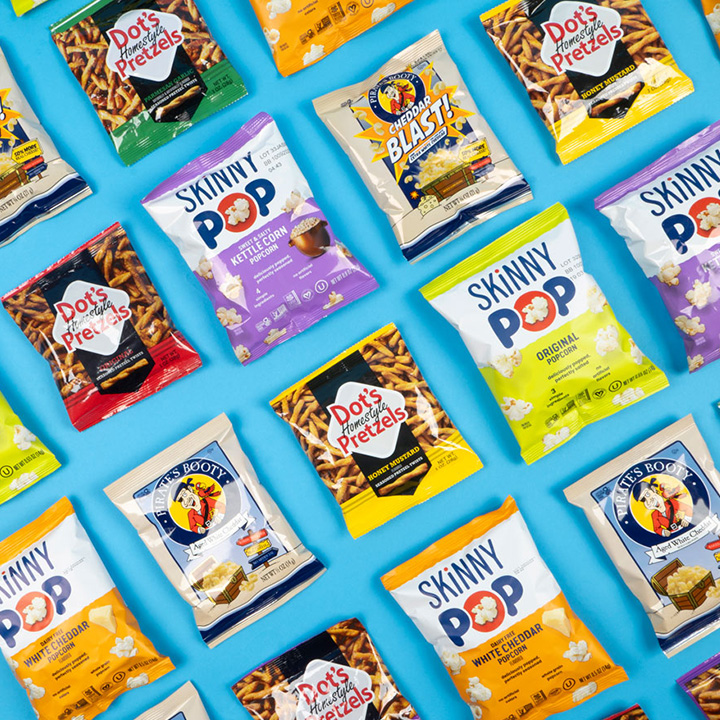 Promotional graphic featuring assorted individual serving size bags of pretzels, popcorn and puff snacks on a blue background