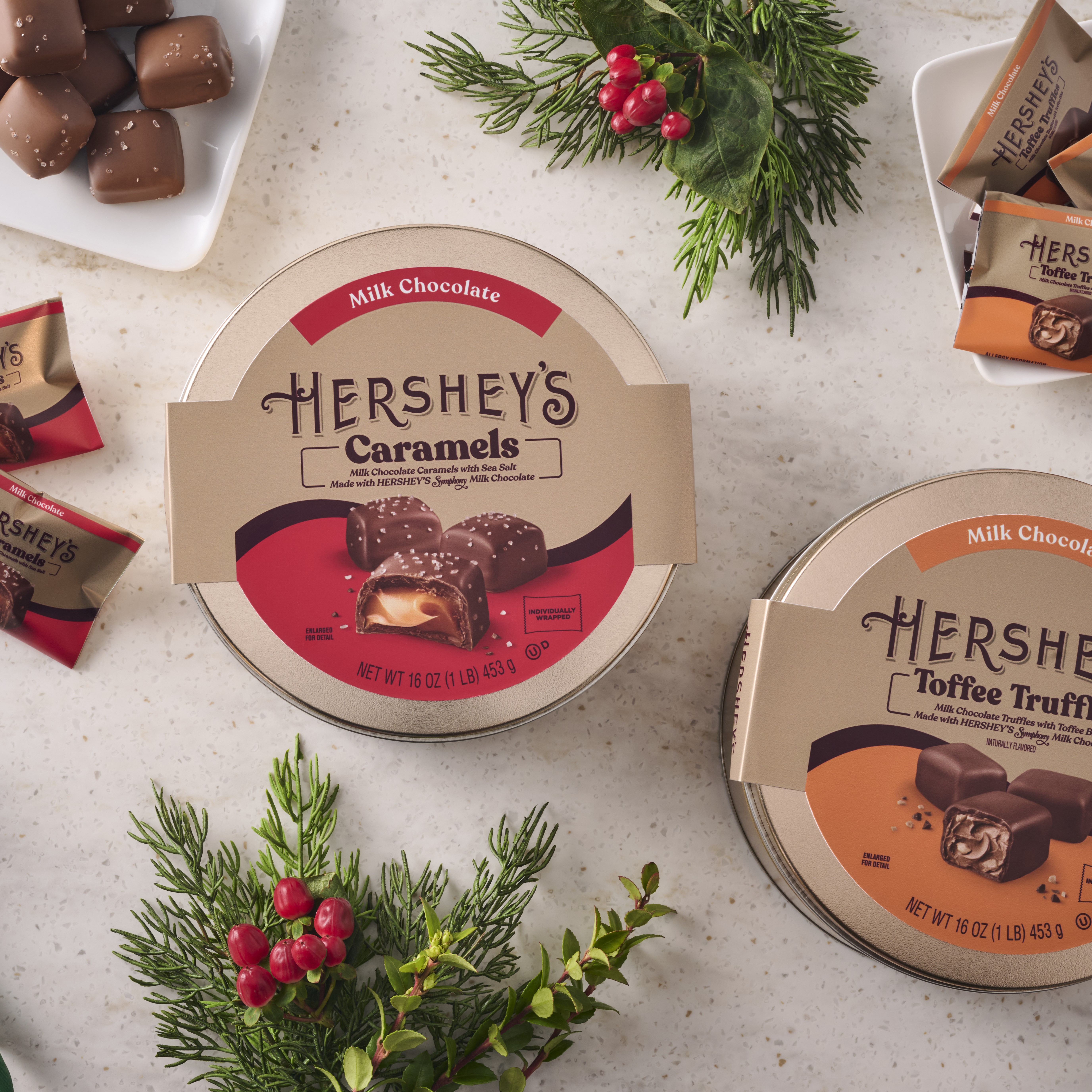 HERSHEY'S Caramels and Toffee Truffles-filled gift tins on a marble countertop adorned with holiday-themed decor